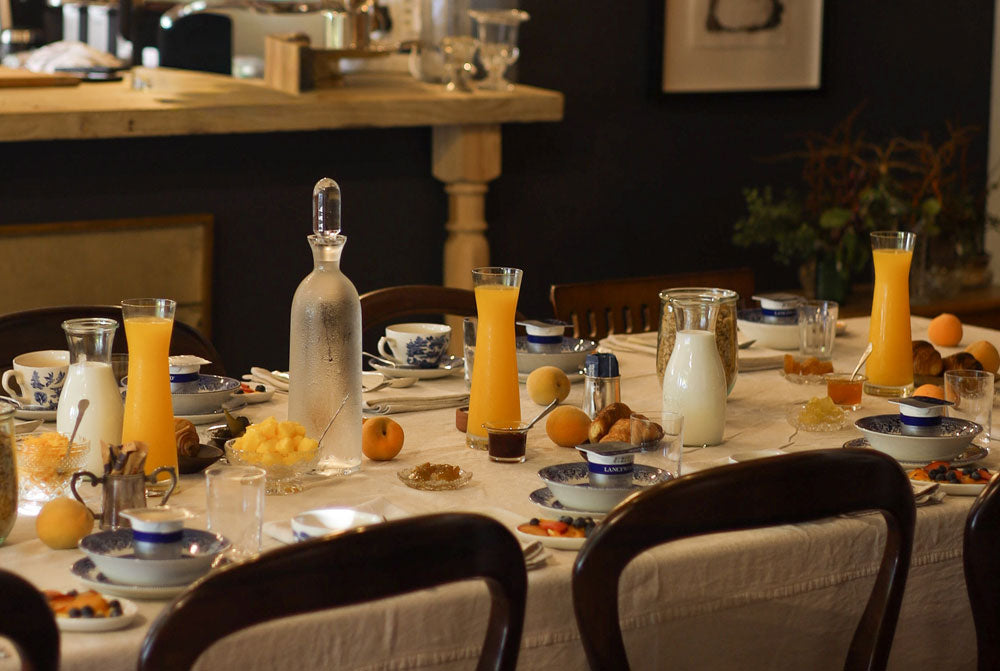 A beautifully set dining table for breakfast, featuring glassware, milk bottles, glasses of orange juice, and fresh oranges.